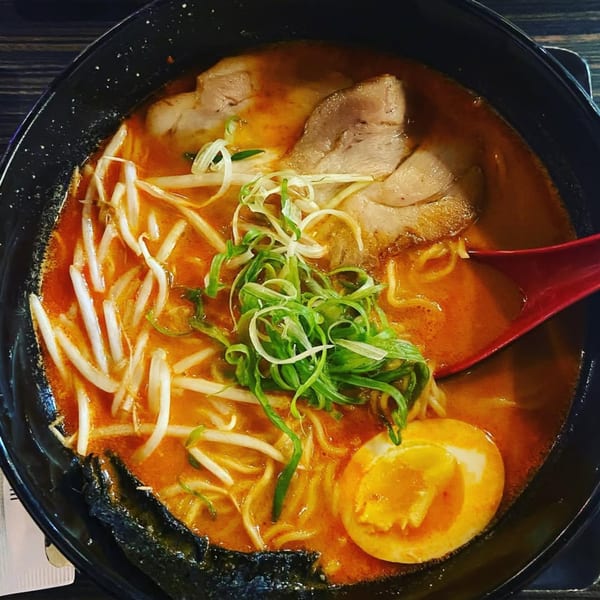 Spicy ramen with pork, bean sprouts, green onions, and a soft-boiled egg in a black bowl.