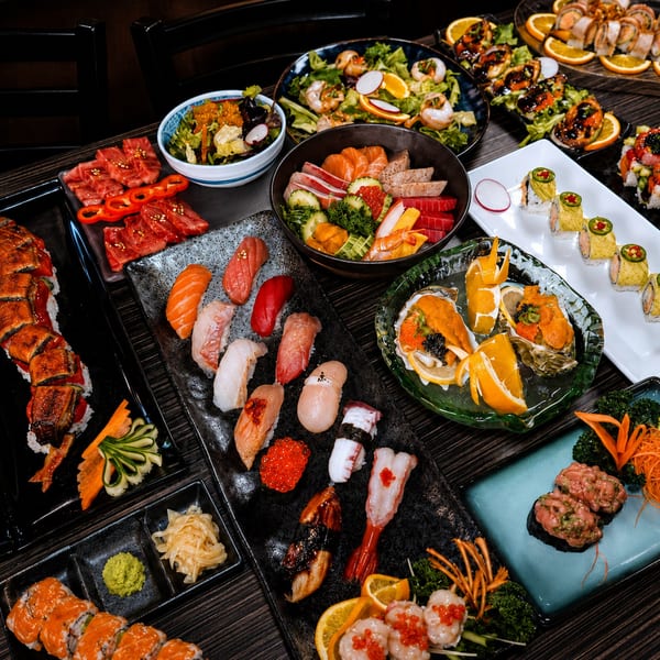 A large spread of various sushi, sashimi, salads, and oysters on a dark wooden table.