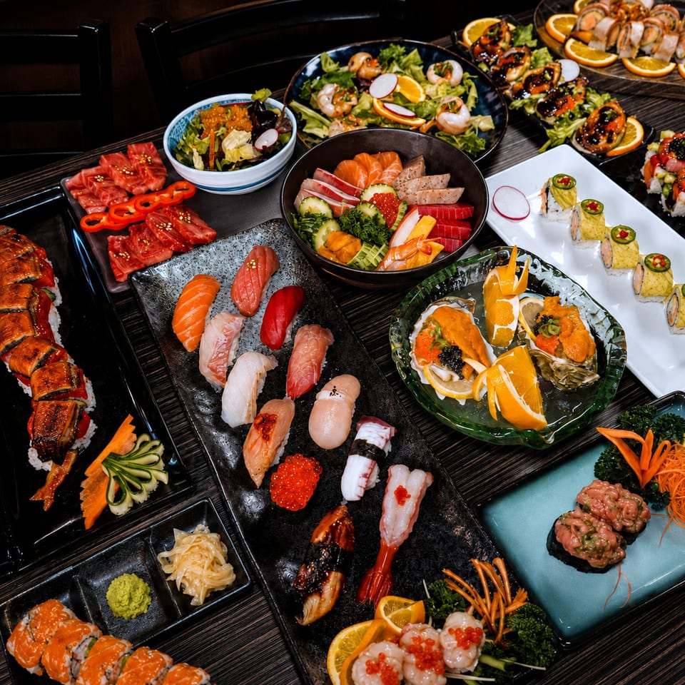 A large spread of various sushi, sashimi, salads, and oysters on a dark wooden table.
