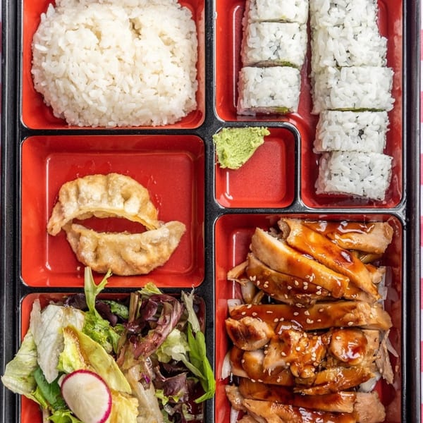 Sushiya bento box with white rice, sushi rolls, gyoza, teriyaki chicken, and a fresh salad.