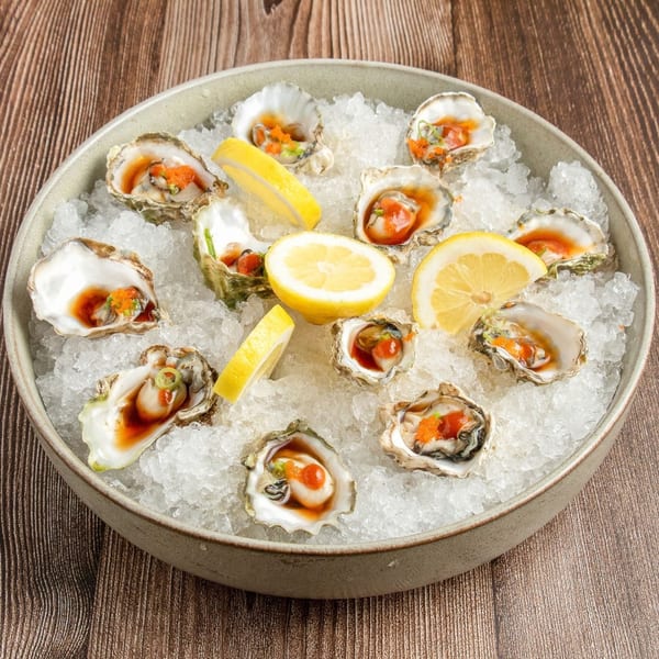 A dozen fresh oysters on the half shell, served on a bed of ice with lemon wedges.