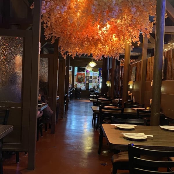 Sushiya's dining room with dark wood booths, tables set with plates and chopsticks, and orange floral ceiling decor.
