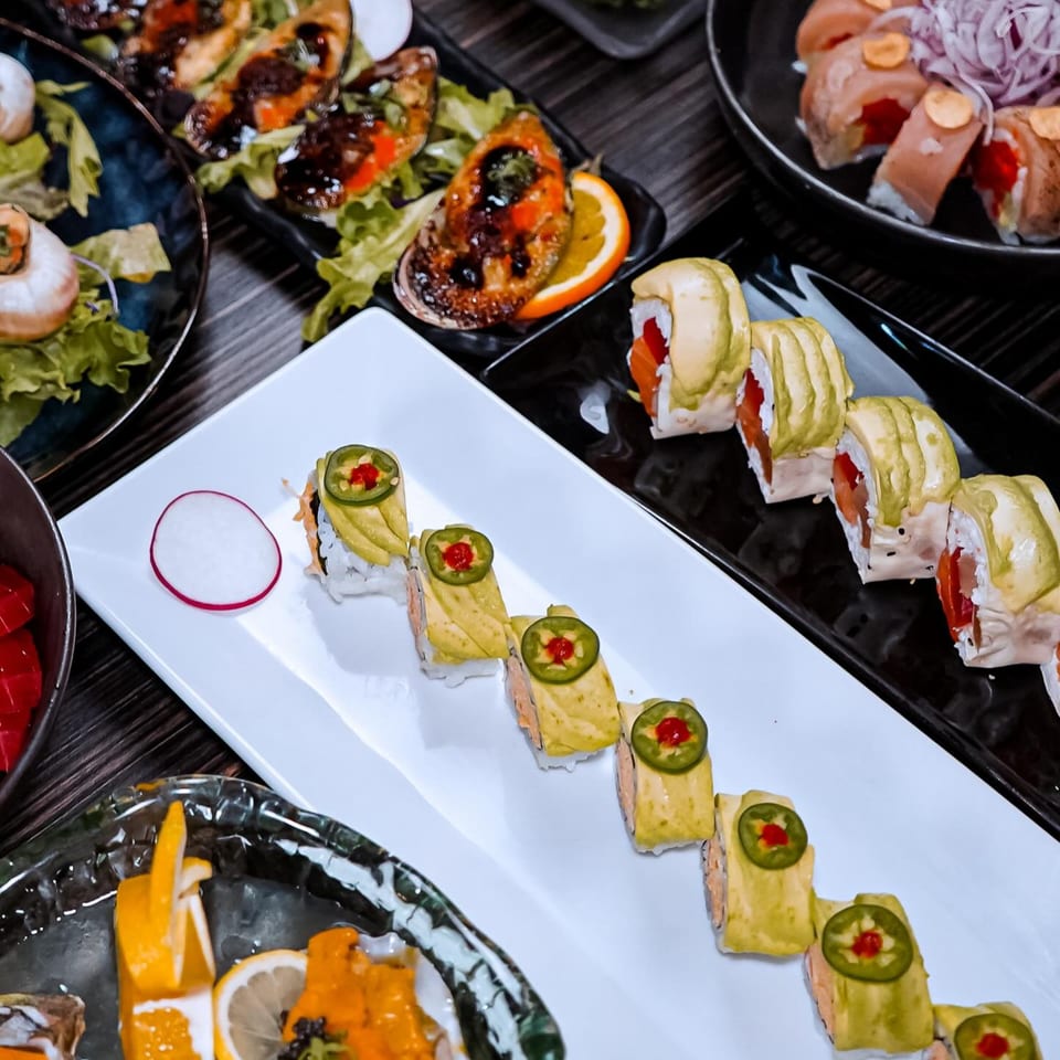 Sushiya's sushi rolls with avocado and jalapeño, alongside other seafood dishes on a dark table.