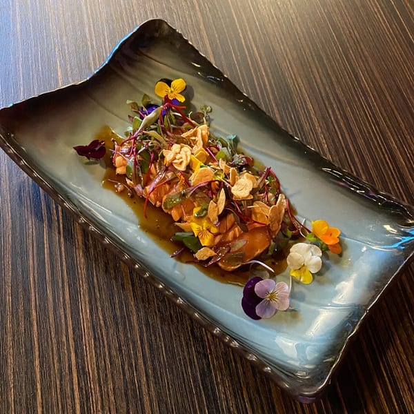 Sushiya's salmon sashimi with microgreens, crispy garlic, and edible flowers on a blue-grey plate.