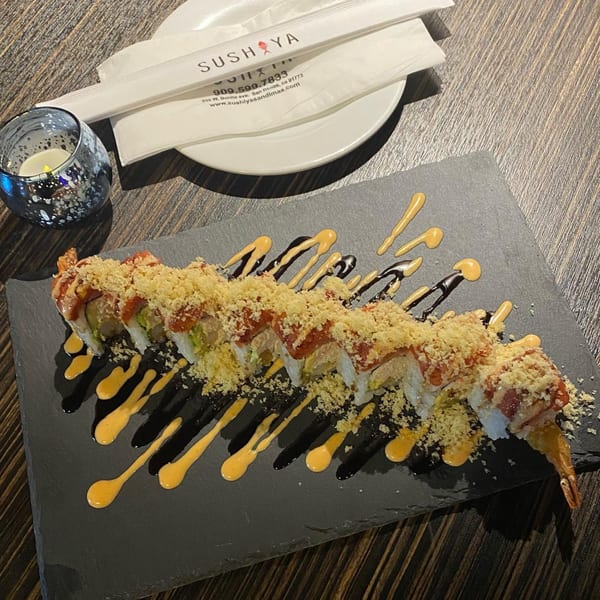 Sushiya sushi roll with crunchy topping and sauces on a slate plate, with chopsticks and candle.