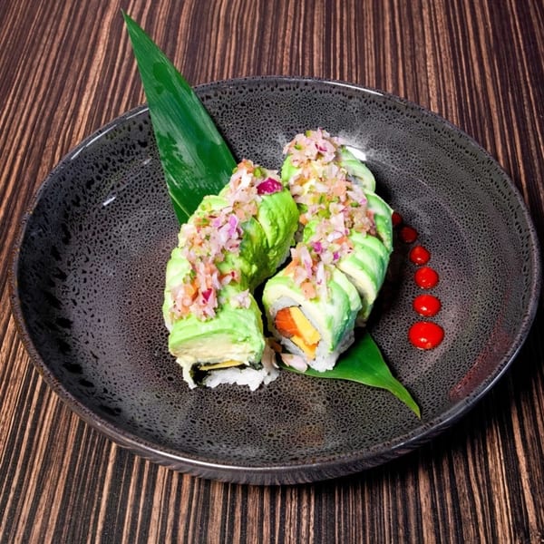 Sushiya's avocado sushi rolls with chopped topping and red sauce dots on a dark plate.