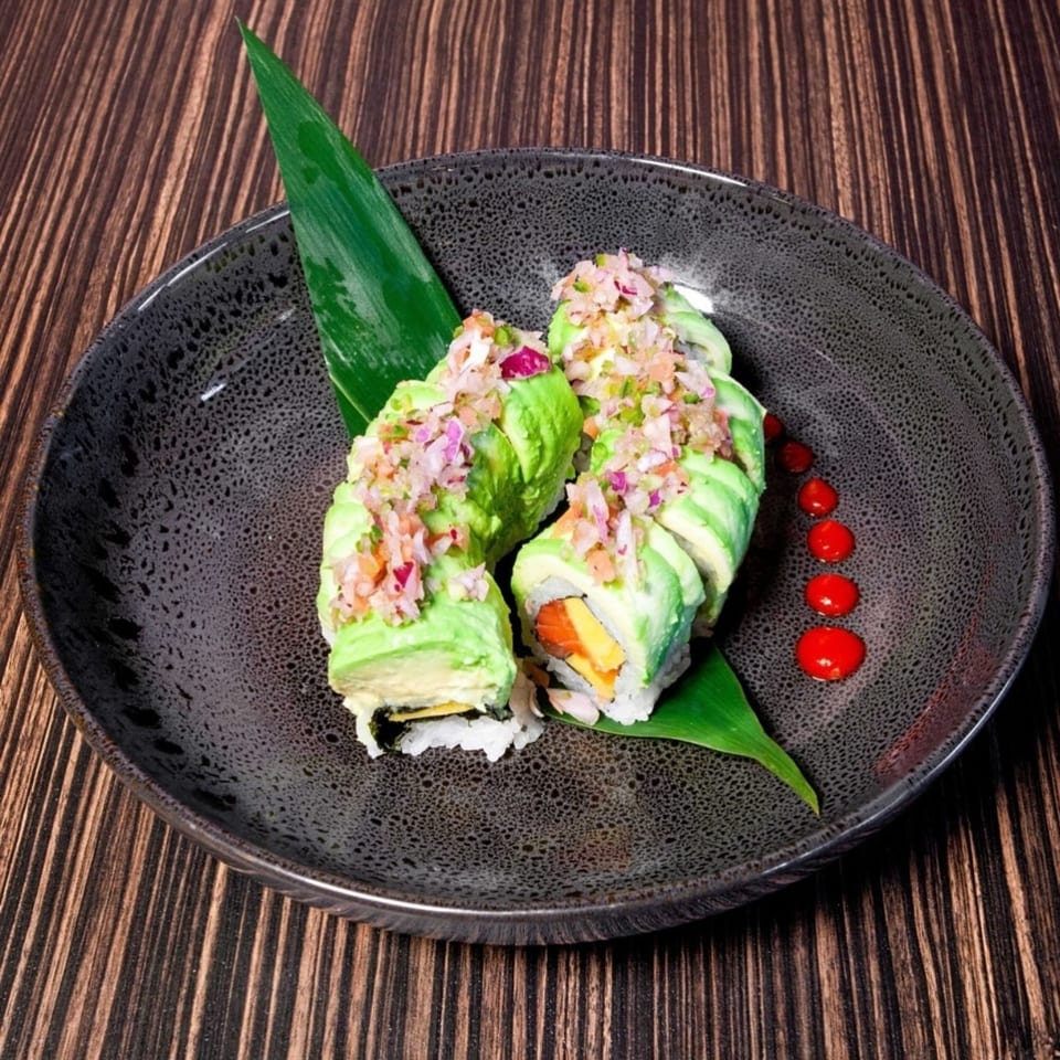 Sushiya's avocado sushi rolls with chopped topping and red sauce dots on a dark plate.