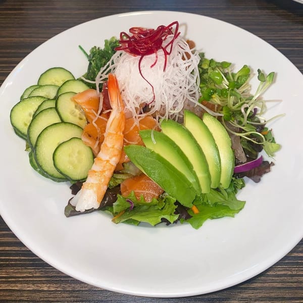 Sushiya's fresh salad with shrimp, salmon, avocado, cucumbers, and mixed greens on a white plate.