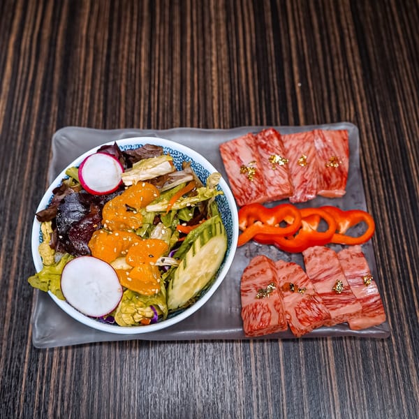 A bowl of fresh salad with radishes and oranges, alongside raw wagyu beef slices and red bell peppers.