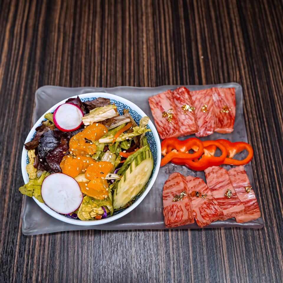A bowl of fresh salad with radishes and oranges, alongside raw wagyu beef slices and red bell peppers.