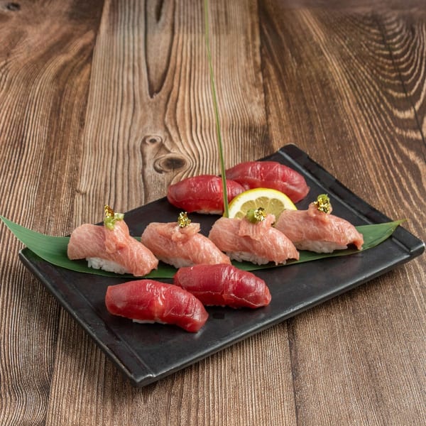 Assortment of tuna nigiri sushi, including lean and fatty cuts, garnished with gold flakes and lemon.