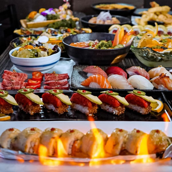 A lavish spread of Sushiya's sushi, sashimi, and other Japanese dishes, with a flaming sushi roll in the foreground.