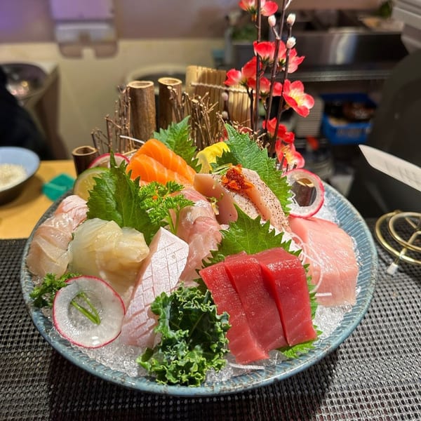 A large platter of assorted sashimi, including tuna, salmon, and white fish, garnished with greens and flowers.