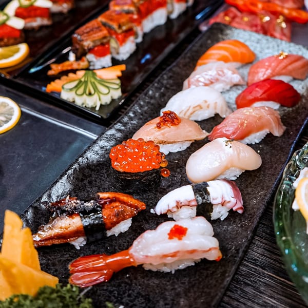 A black platter of various Sushiya sushi and sashimi, including salmon, tuna, eel, and roe.