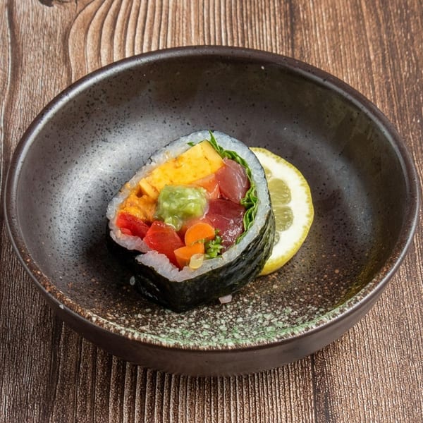 A colorful sushi hand roll with tuna, avocado, red peppers, and egg, served with a lemon slice.
