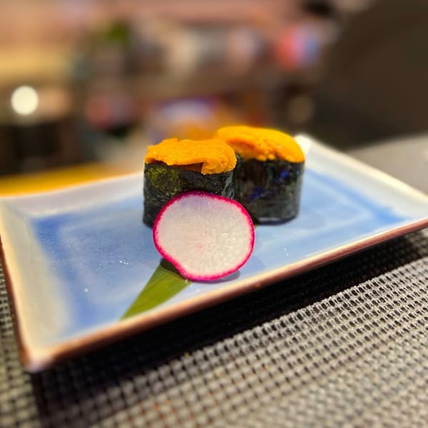 Two pieces of uni sushi with a slice of radish on a blue and white rectangular plate.