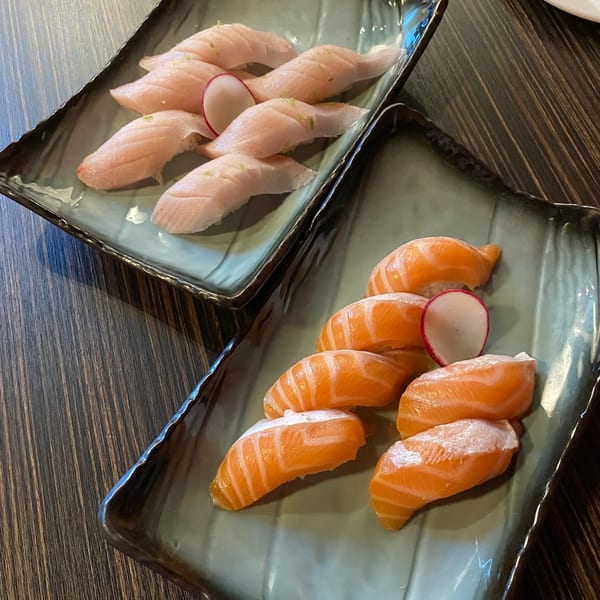 Two plates of Sushiya nigiri, one with salmon and the other with white fish, on a wooden table.