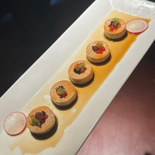 Five round sushi pieces with colorful roe and sauce on a white rectangular plate with radish slices.