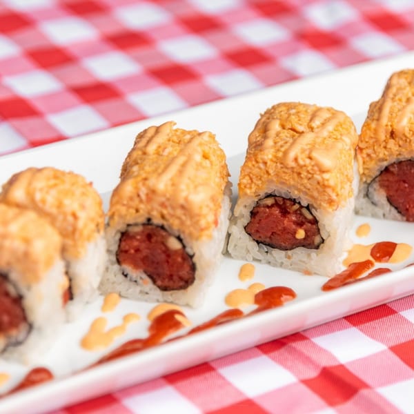 Sushiya's spicy tuna rolls with orange sauce drizzle on a white plate over a red and white checkered tablecloth.