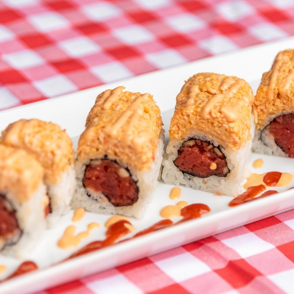 Sushiya's spicy tuna rolls with orange sauce drizzle on a white plate over a red and white checkered tablecloth.