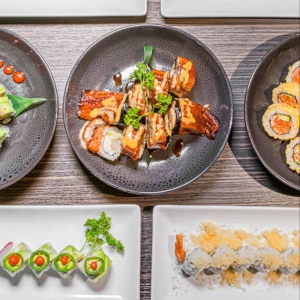 Overhead view of various sushi rolls on dark and white plates, including eel, spicy salmon, and jalapeño.