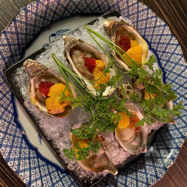 Sushiya's fresh oysters on ice, topped with bright orange uni, red roe, and green garnish.